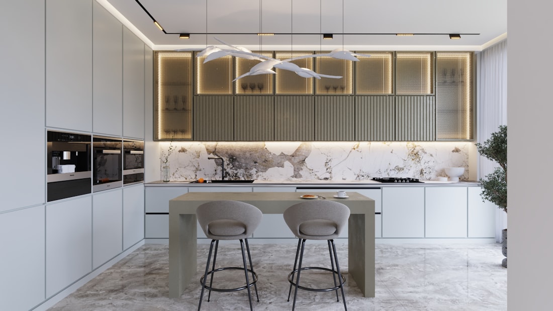 Cocina blanca con isla central, encimera de piedra y taburetes.