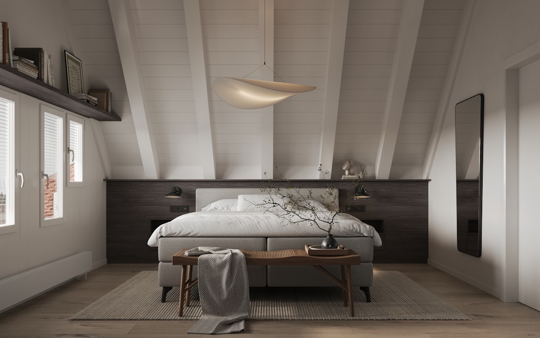Dormitorio con cabecero de madera, ropa de cama clara y techo abuhardillado.