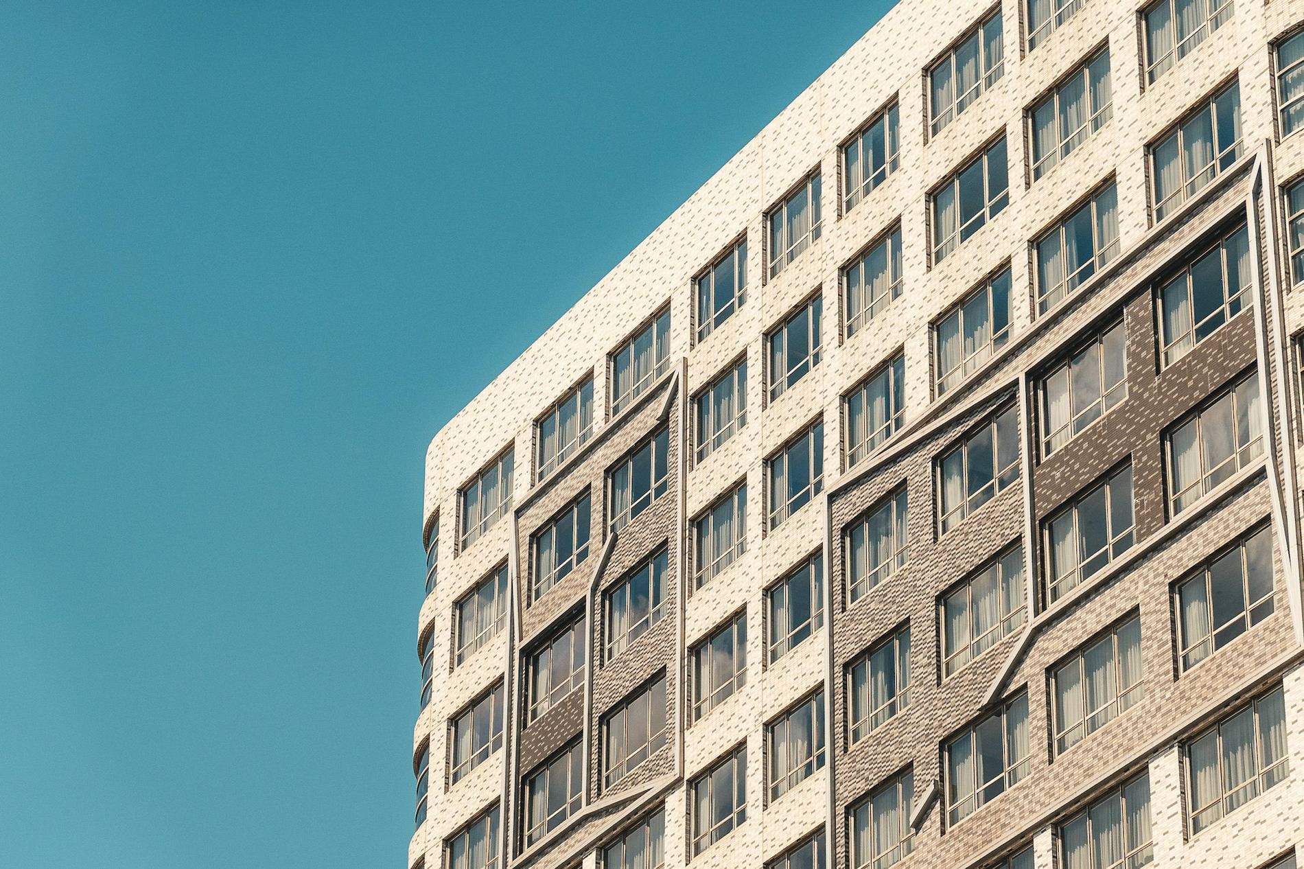 Fachada de un edificio de viviendas en diagonal recortada contra un cielo azul despejado.