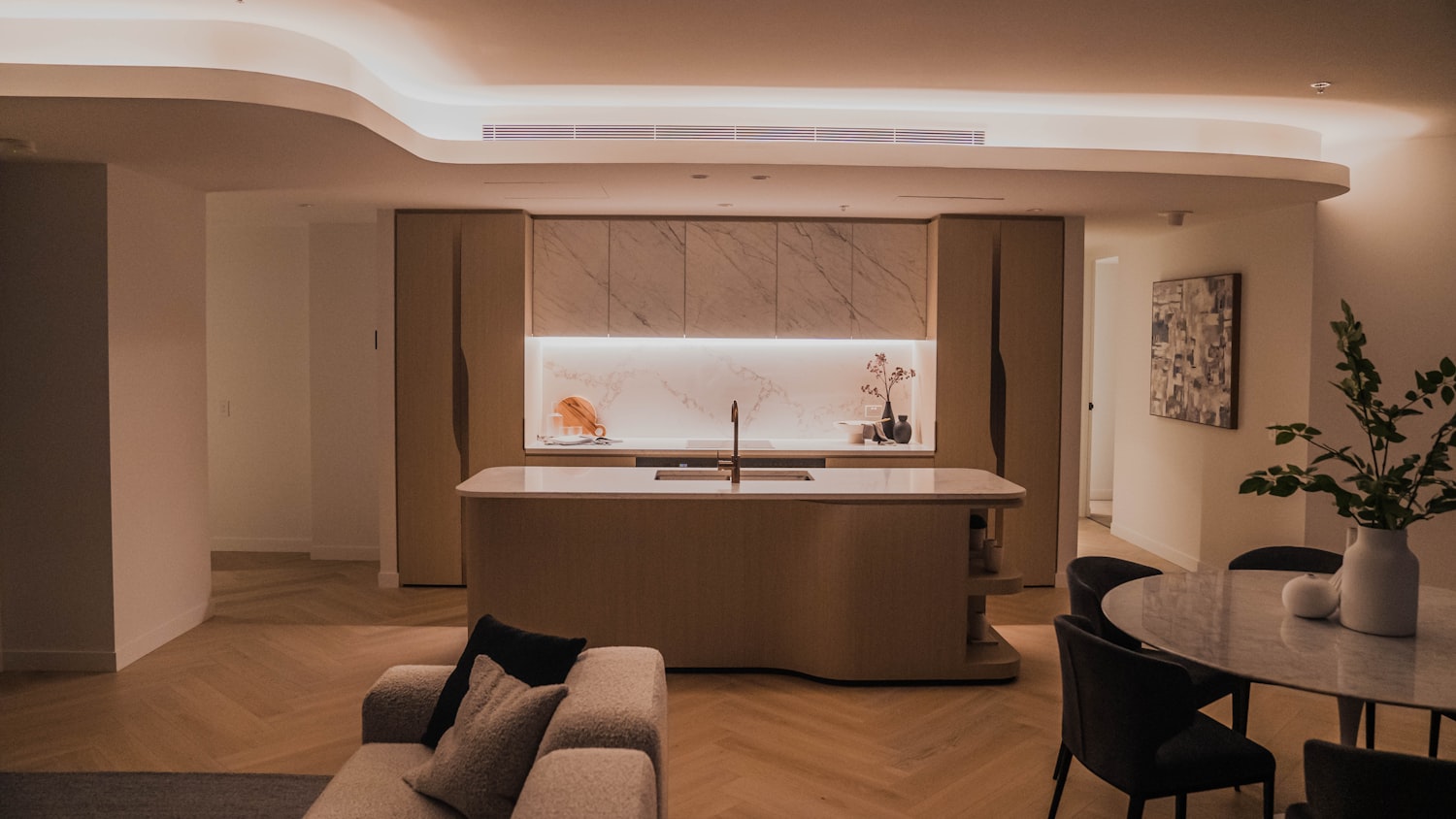 Salón comedor con sofá claro, mesa de comedor y cocina integrada al fondo.